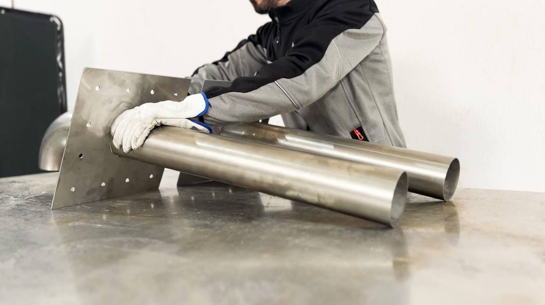 Worker in gloves handling stainless steel pipes and plate